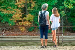 Grandmother wearing backpack with granddaughter, outdoors conversing